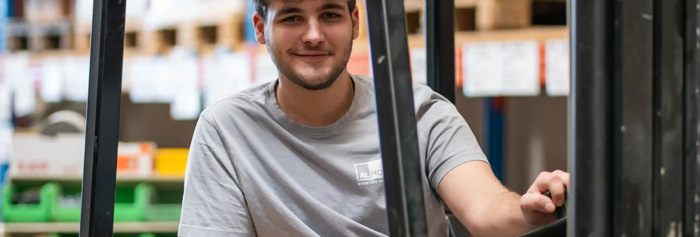 Person auf einem Gabelstapler in einer Lagerhalle. Im Hintergrund befinden sich Regale, Lagerflächen und Materialien für die Logistik.