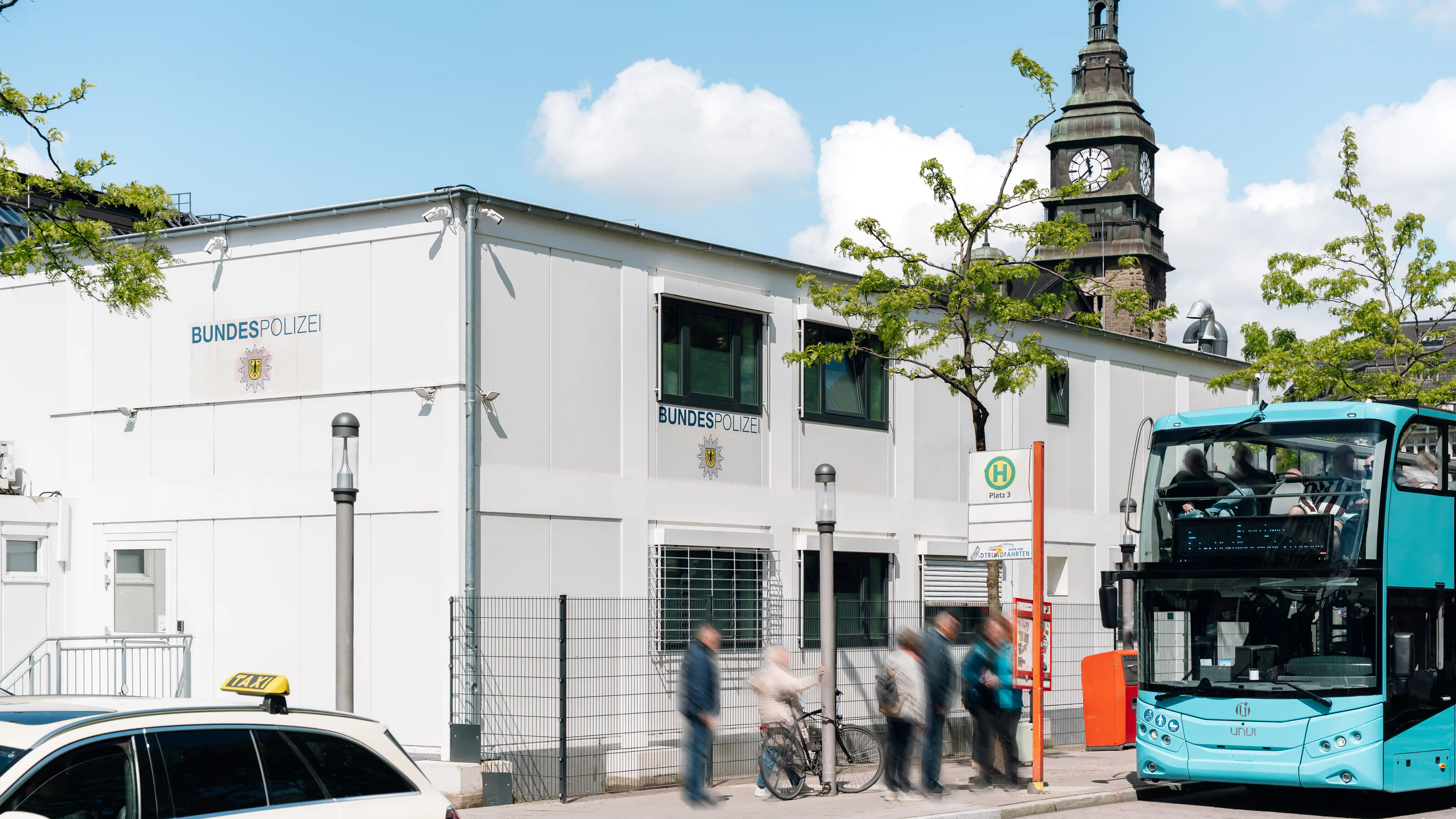 Dienstgebäude der Bundespolizei in zentraler Lage am Hamburger Hauptbahnhof mit Bushaltestelle und historischem Kirchturm im Hintergrund.