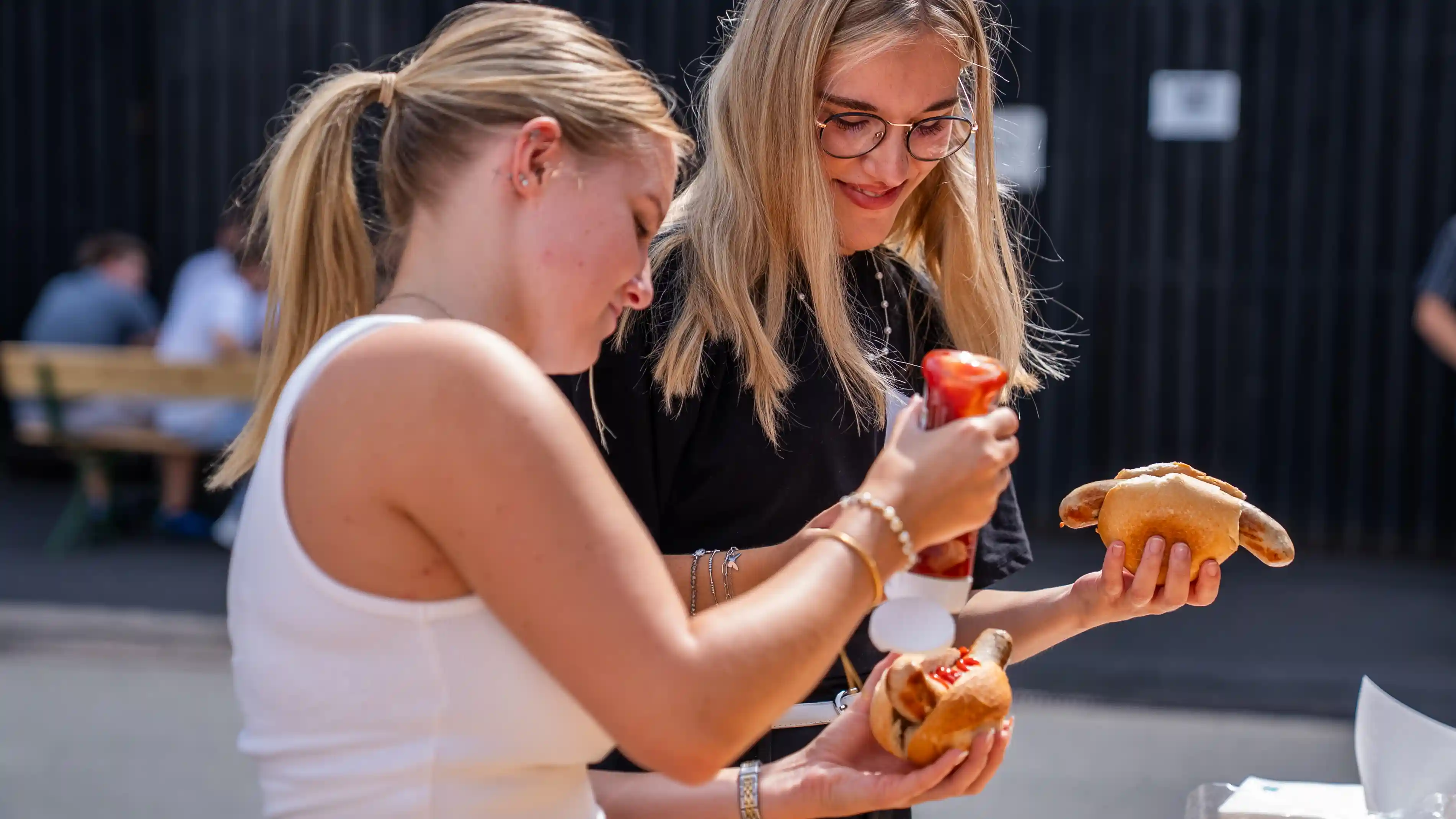 Zwei junge Frauen bereiten sich im Freien Bratwurst mit Ketchup zu