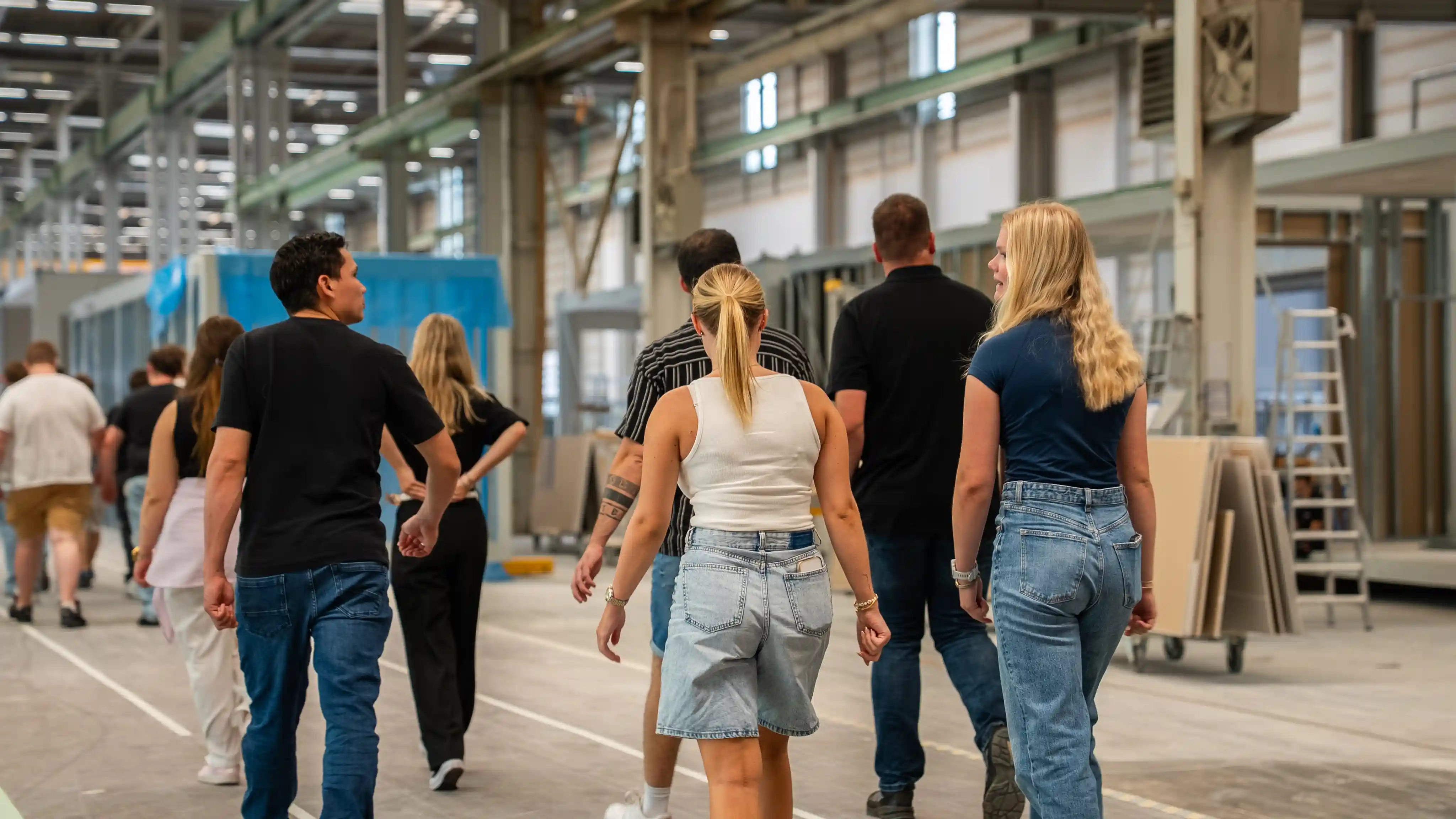 Gruppe von Auszubildenden und Ausbildern geht durch die Produktionshalle bei einer Werksführung