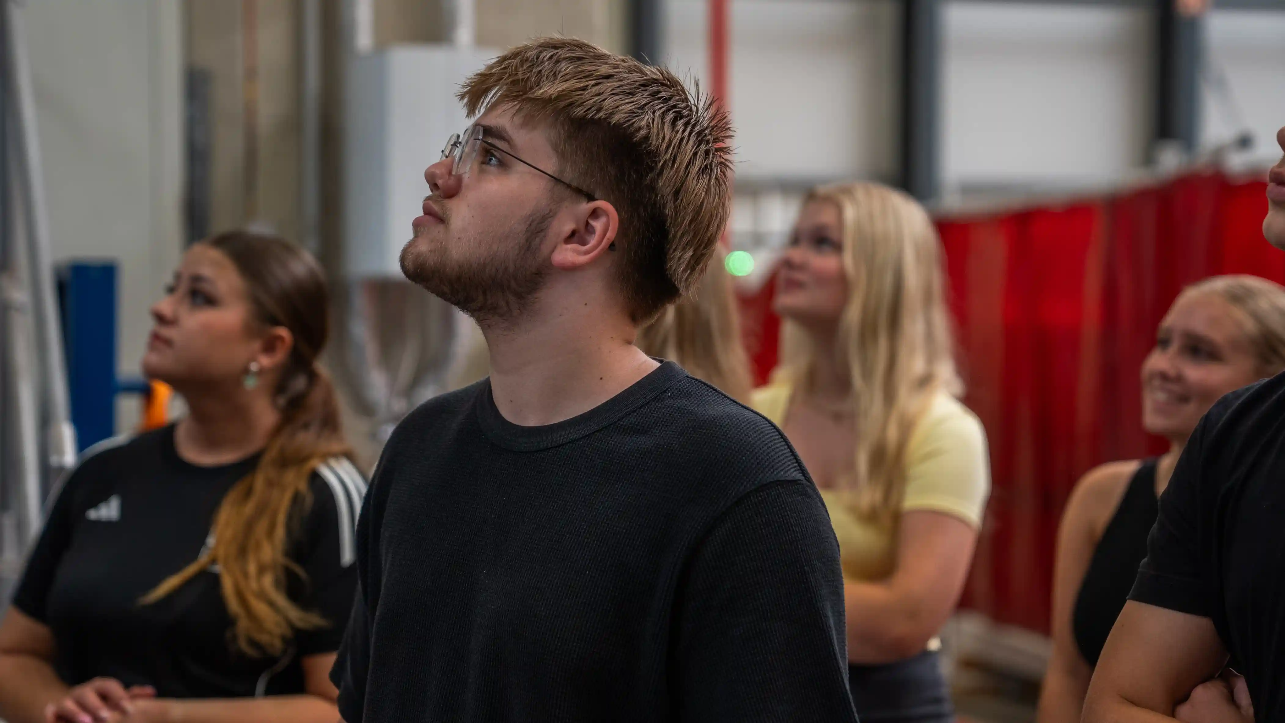 Ein Auszubildender blickt in der Werkshalle nach oben, im Hintergrund weitere Auszubildende