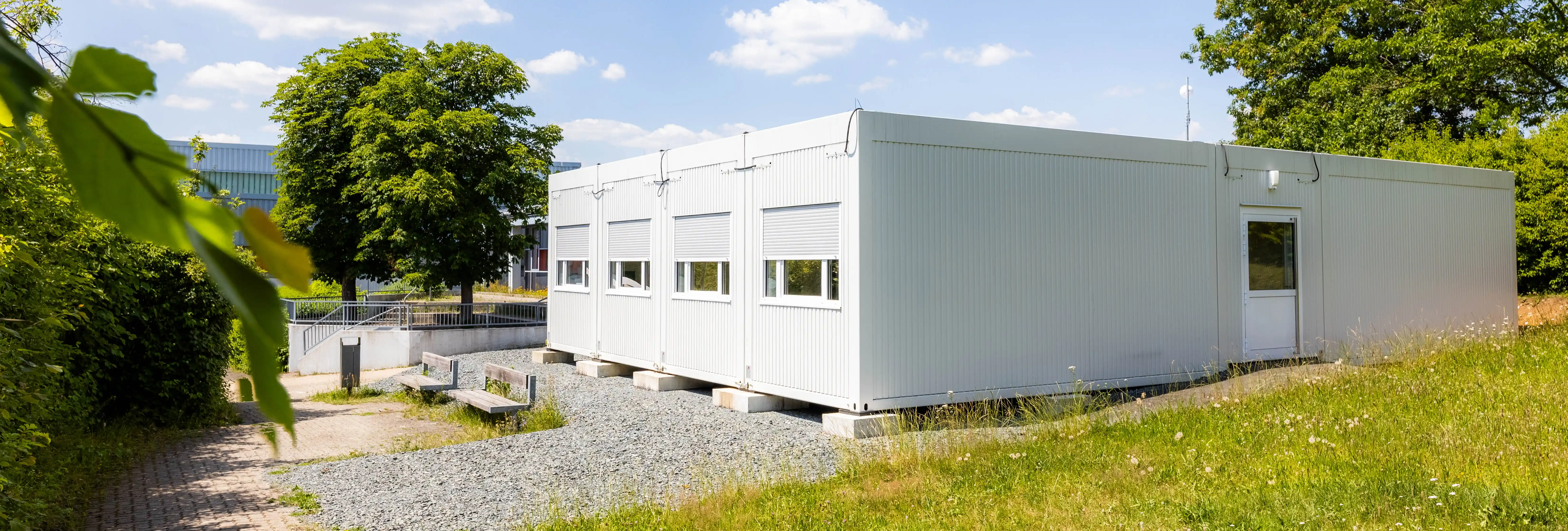 Temporäre Schulcontaineranlage mit mehreren Klassenräumen und Fensterreihen. Die ProENERGY-Anlage befindet sich auf dem Gelände der Pestalozzi-Schule und ist von Grünflächen und Bäumen umgeben.
